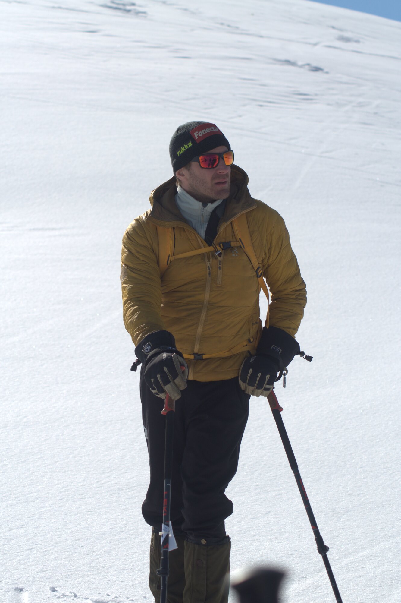 Tommi Haapakangas on a snowy slope with ski poles, yellow jacket and Rukka beanie
